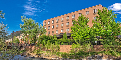 Four story red brick building on hill overlooking creek with blue sky