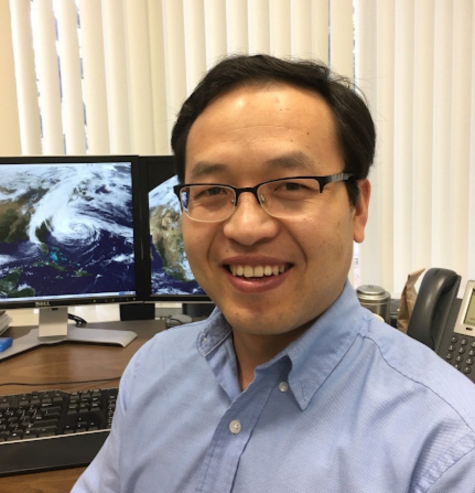 man with glasses in front of computer screens