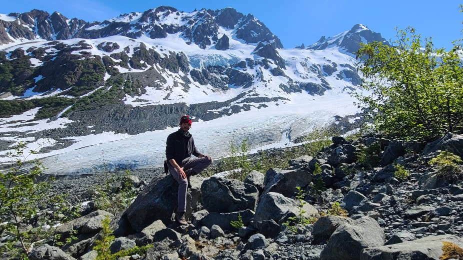 man sitting on rocks with snowy mountains in the background