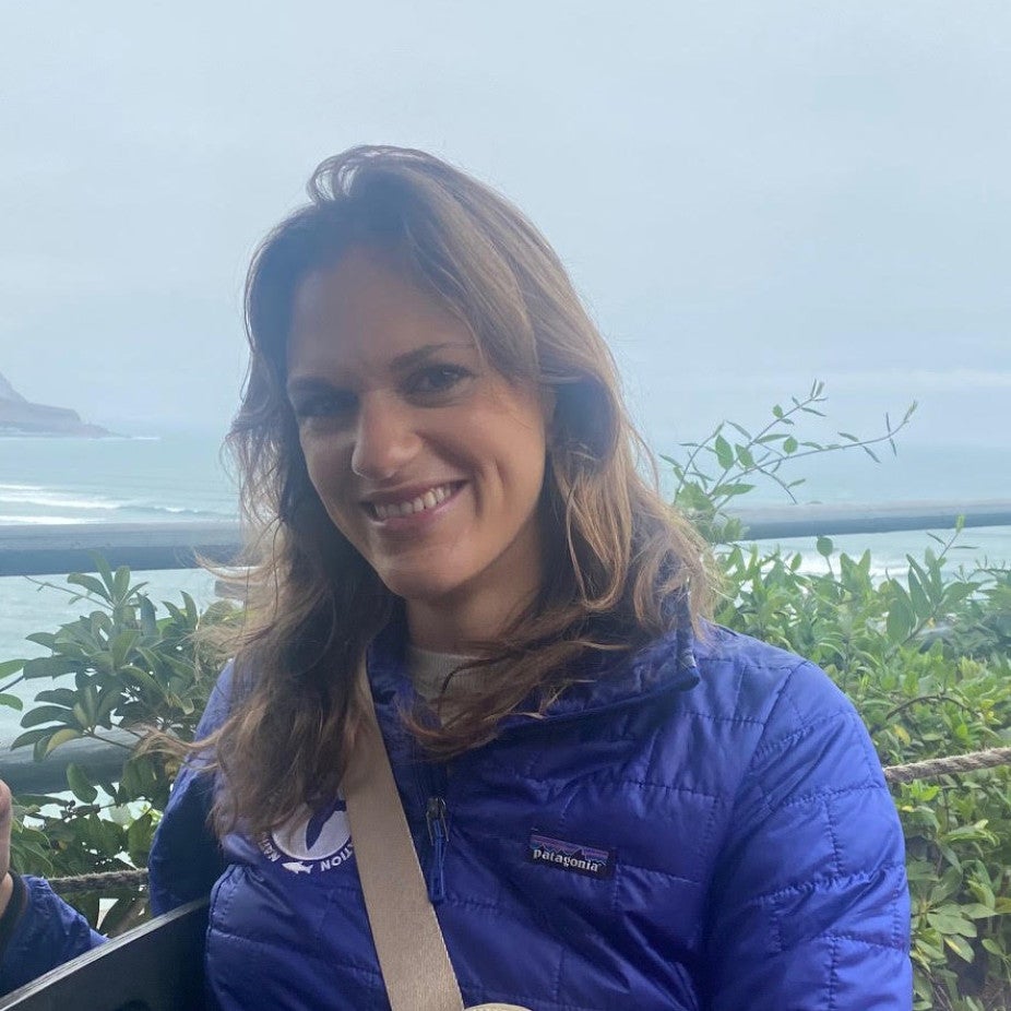 woman with long brown hair wearing a blue shirt in front of misty ocean